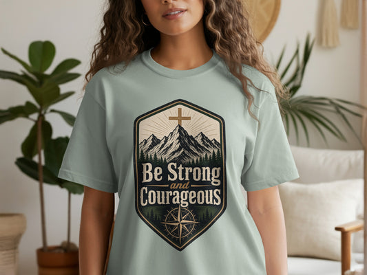 Light green t-shirt with mountains, cross, and compass graphic reading "Be Strong and Courageous."