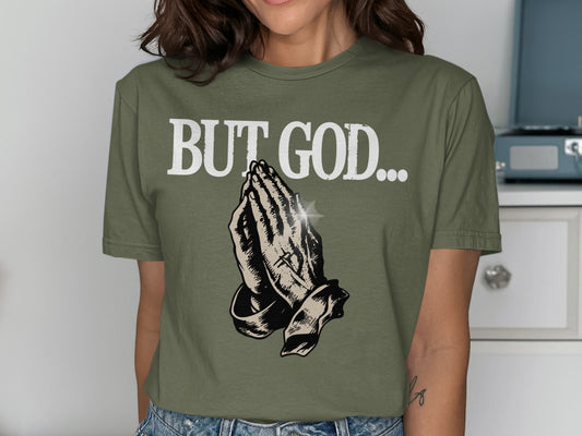 Olive green t-shirt with "BUT GOD..." and praying hands graphic.