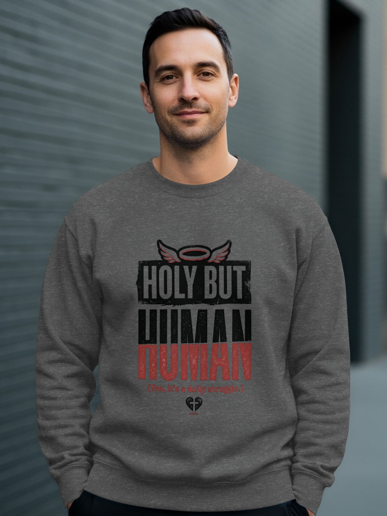 Man wearing a gray sweatshirt with "HOLY BUT HUMAN" text and halo graphic.