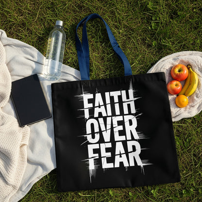 Black tote bag with white "FAITH OVER FEAR" text, on grass with fruit and water.
