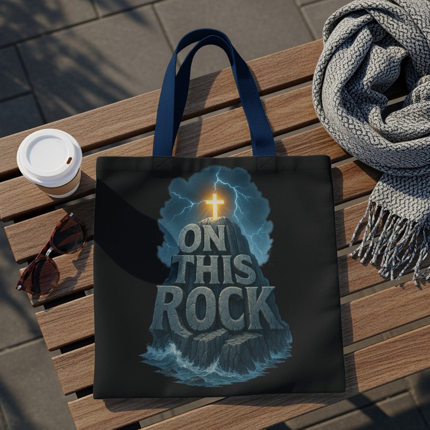 Black tote bag with a distressed graphic of a cross atop a rocky island, with text "ON THIS ROCK".