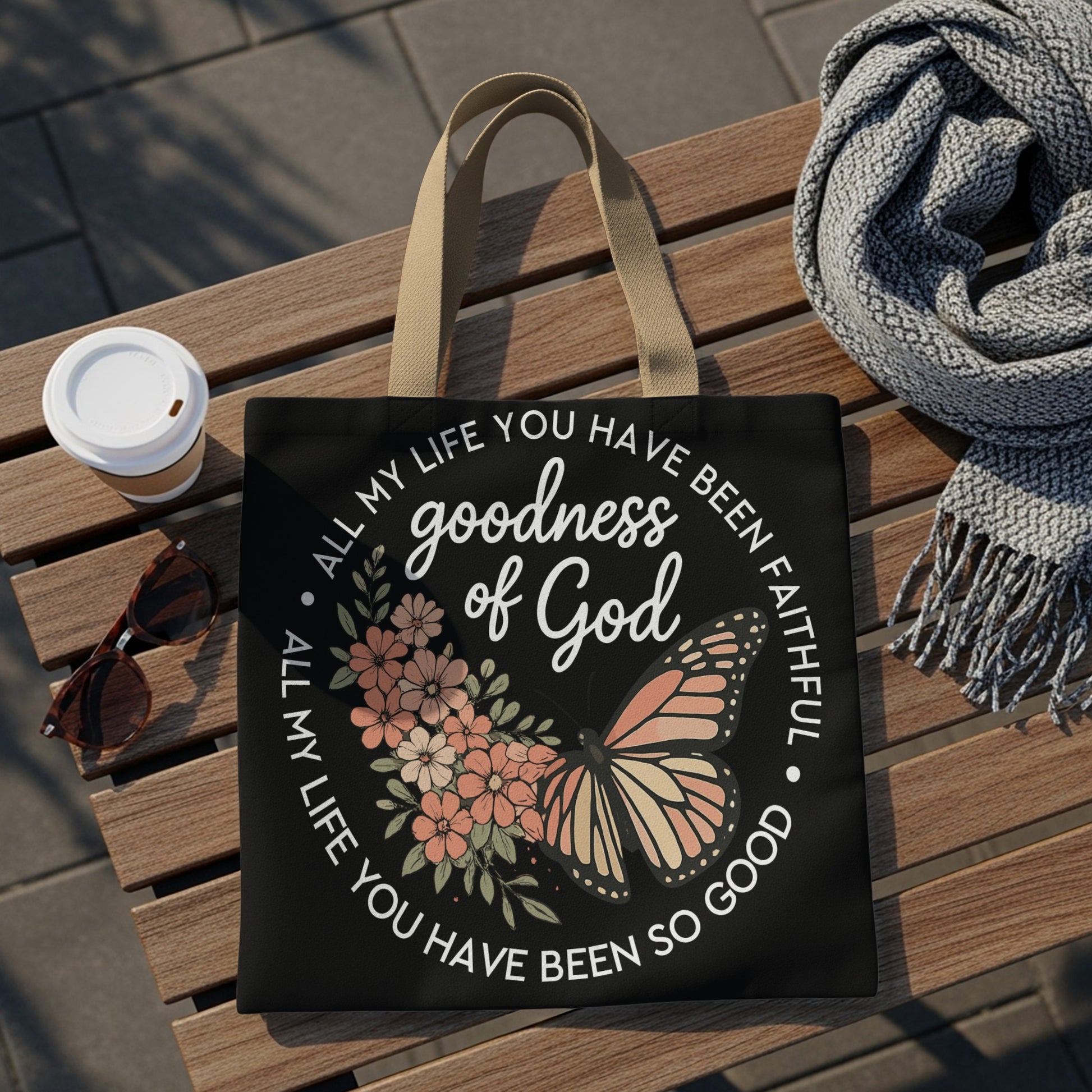 Black tote bag with "Goodness of God" text, floral design, and butterfly.