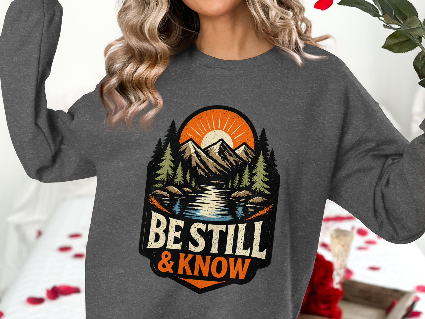 Dark gray sweatshirt with "Be Still & Know" mountain sunset graphic.