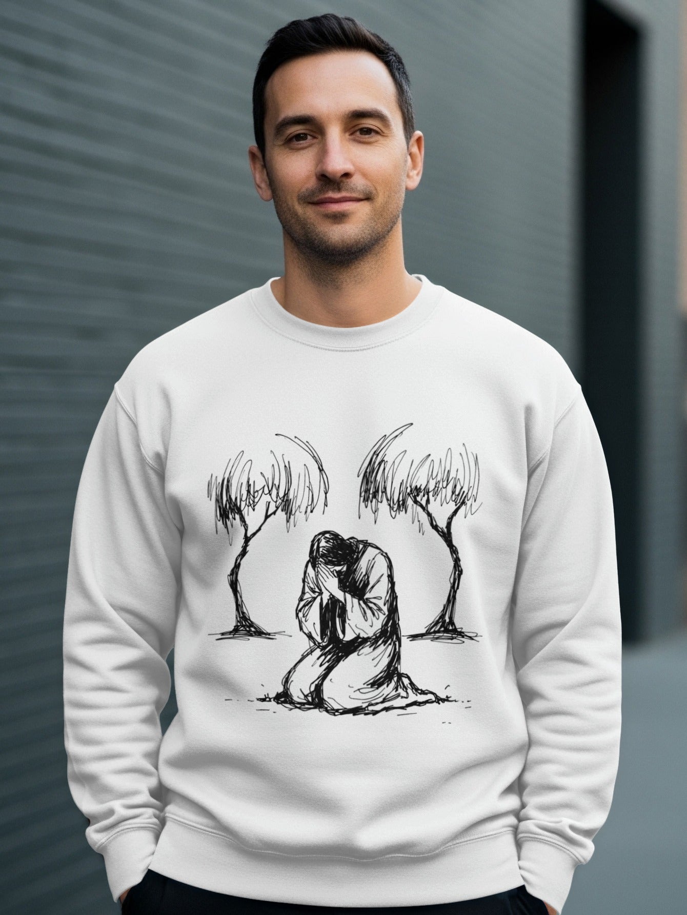 Man wearing white sweatshirt with drawing of Jesus kneeling between two trees.