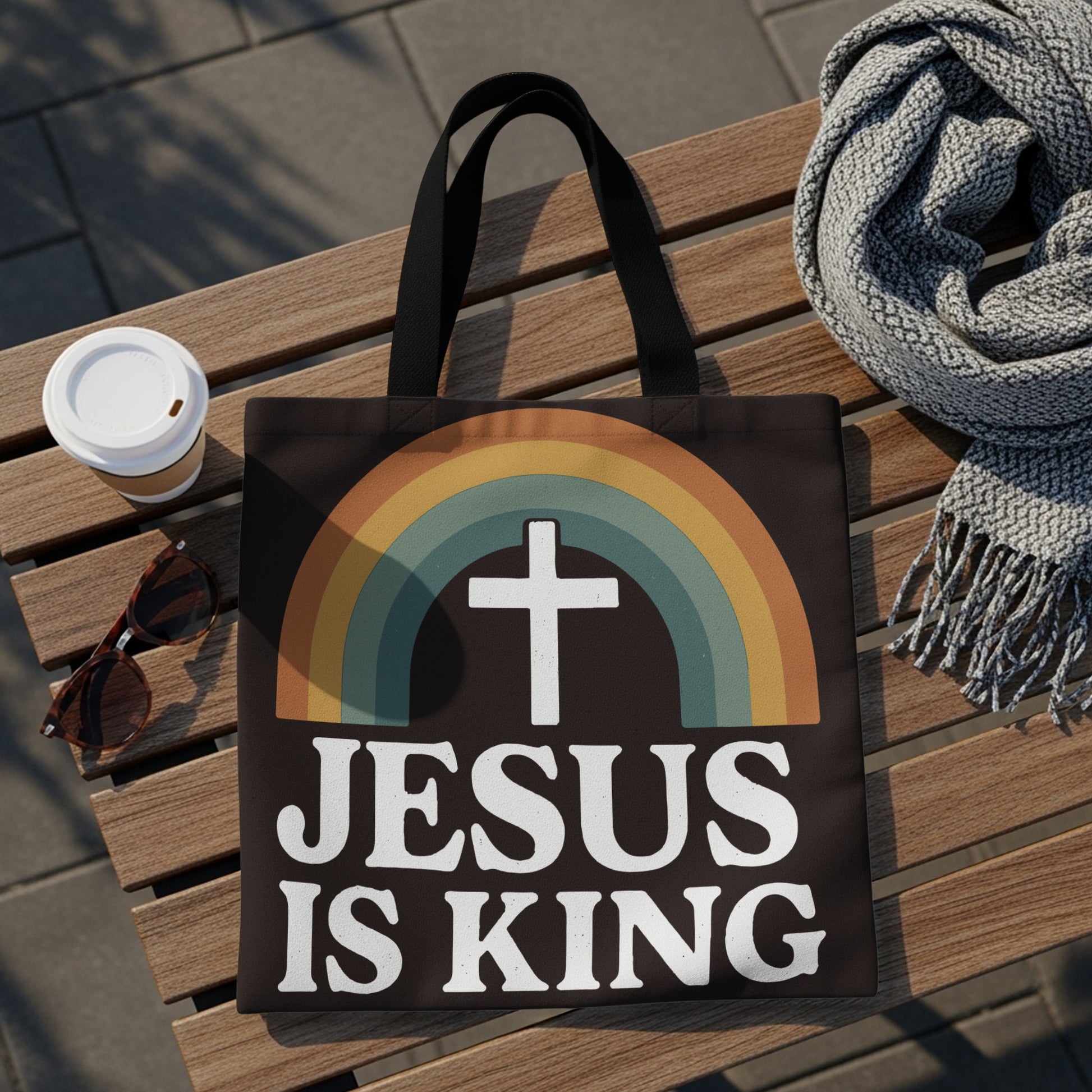 Black tote bag with a white cross and rainbow graphic, reading "JESUS IS KING".
