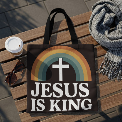 Black tote bag with a white cross and rainbow graphic, reading "JESUS IS KING".