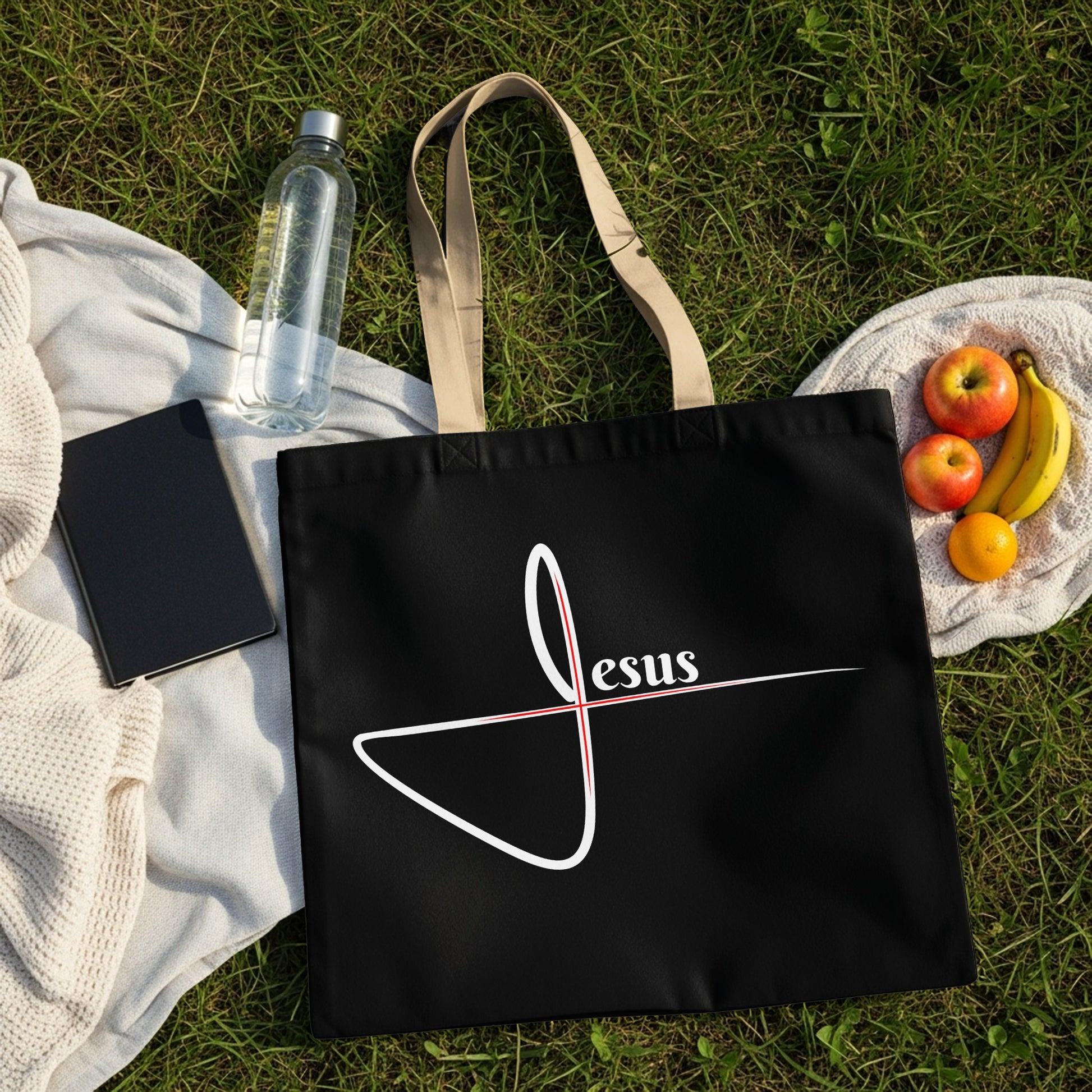 Black tote bag with white "Jesus" text and a red cross symbol.