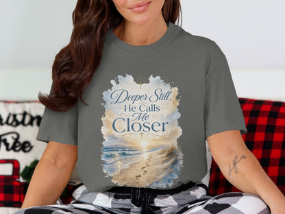 Gray t-shirt with "Deeper Still, He Calls Me Closer" quote and beach scene.