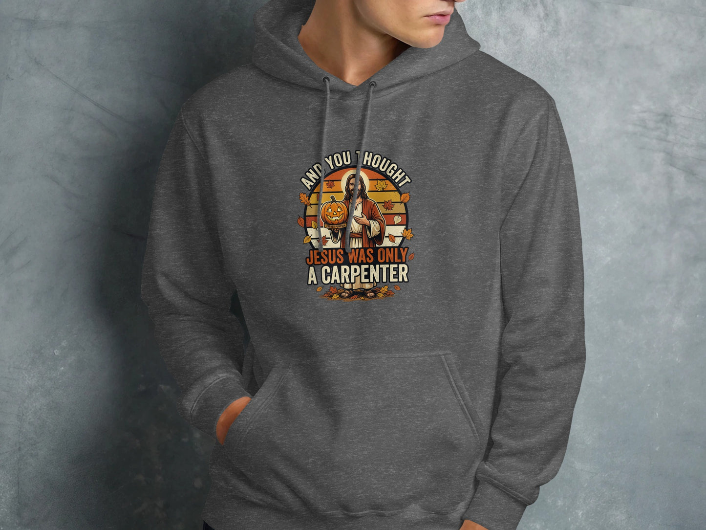 Dark grey hoodie with "And you thought Jesus was only a carpenter" text and pumpkin graphic.