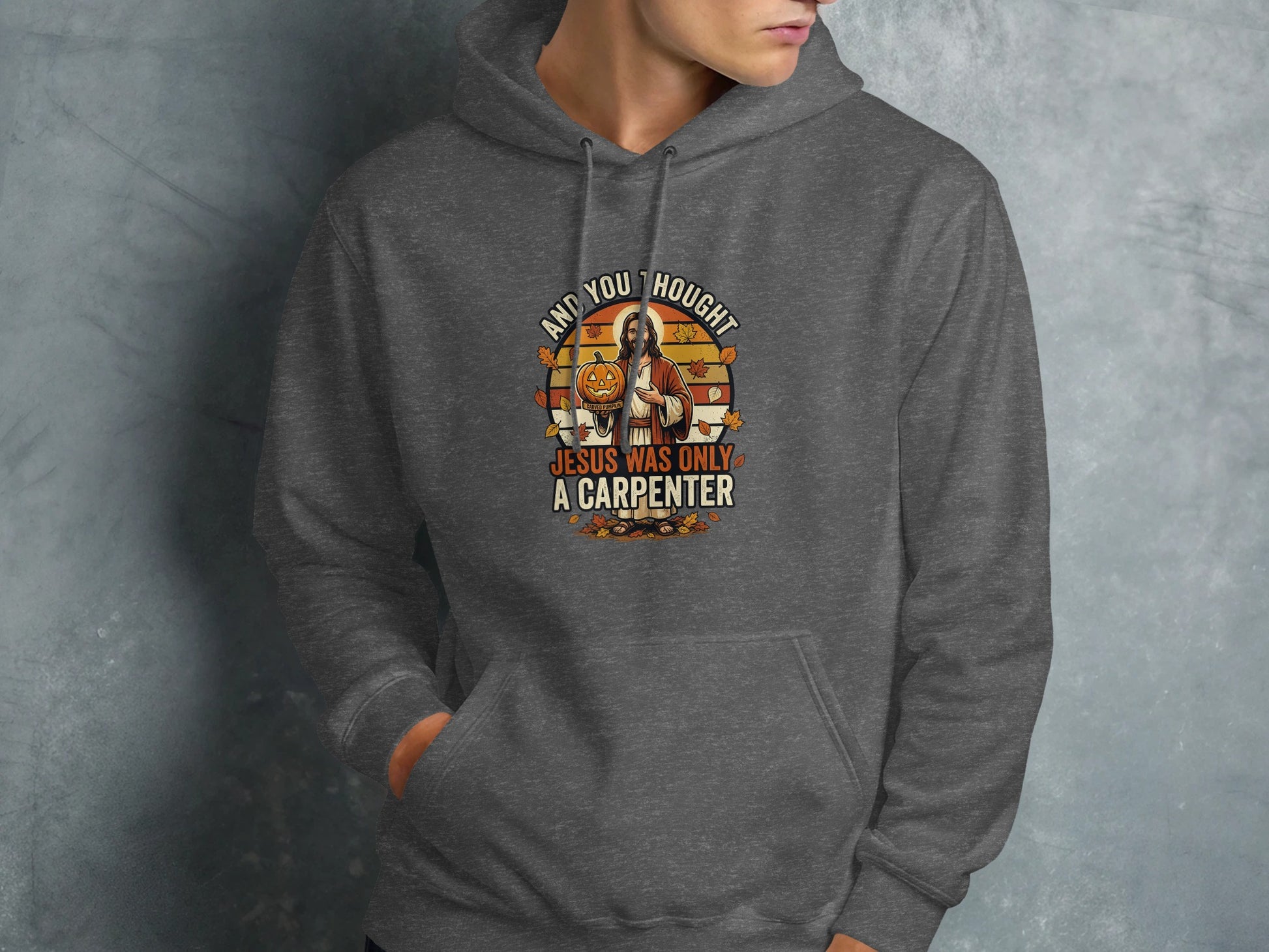 Dark grey hoodie with "And you thought Jesus was only a carpenter" text and pumpkin graphic.
