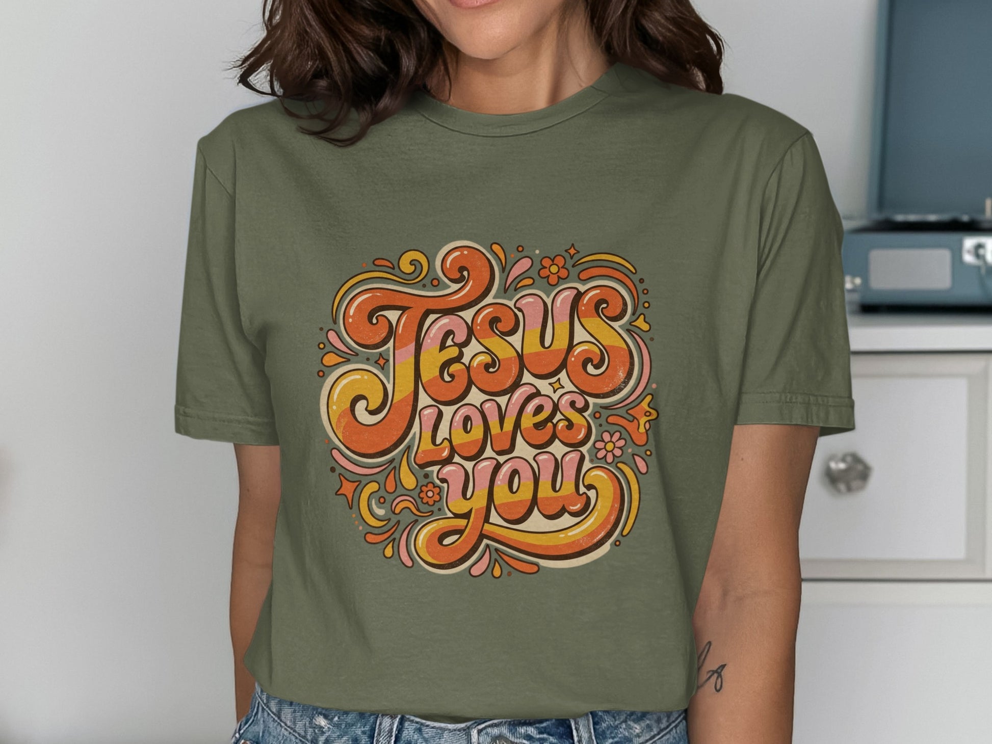 Green t-shirt with "Jesus Loves You" text in retro floral design.