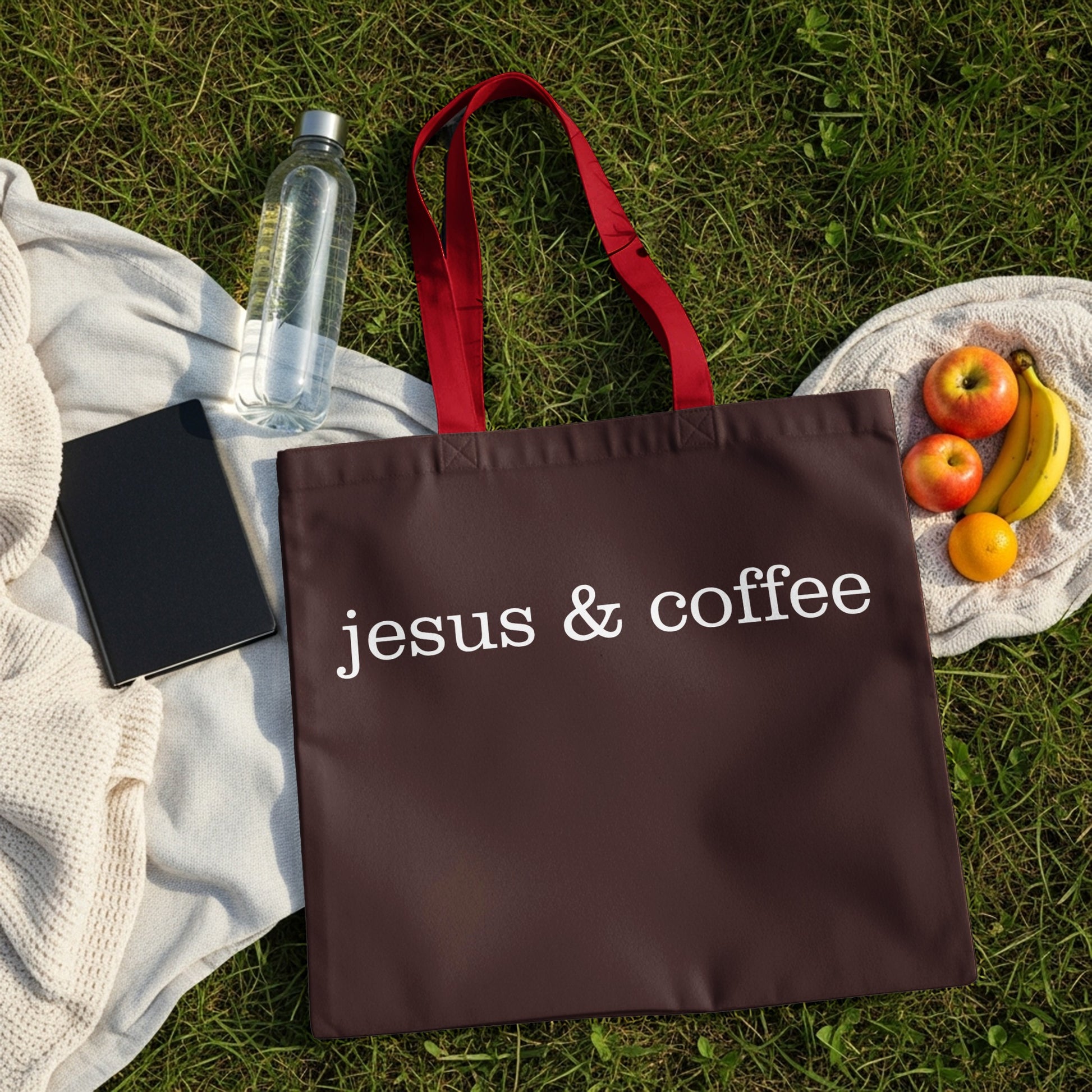 Brown tote bag with "jesus & coffee" text, on a grassy background with fruit.