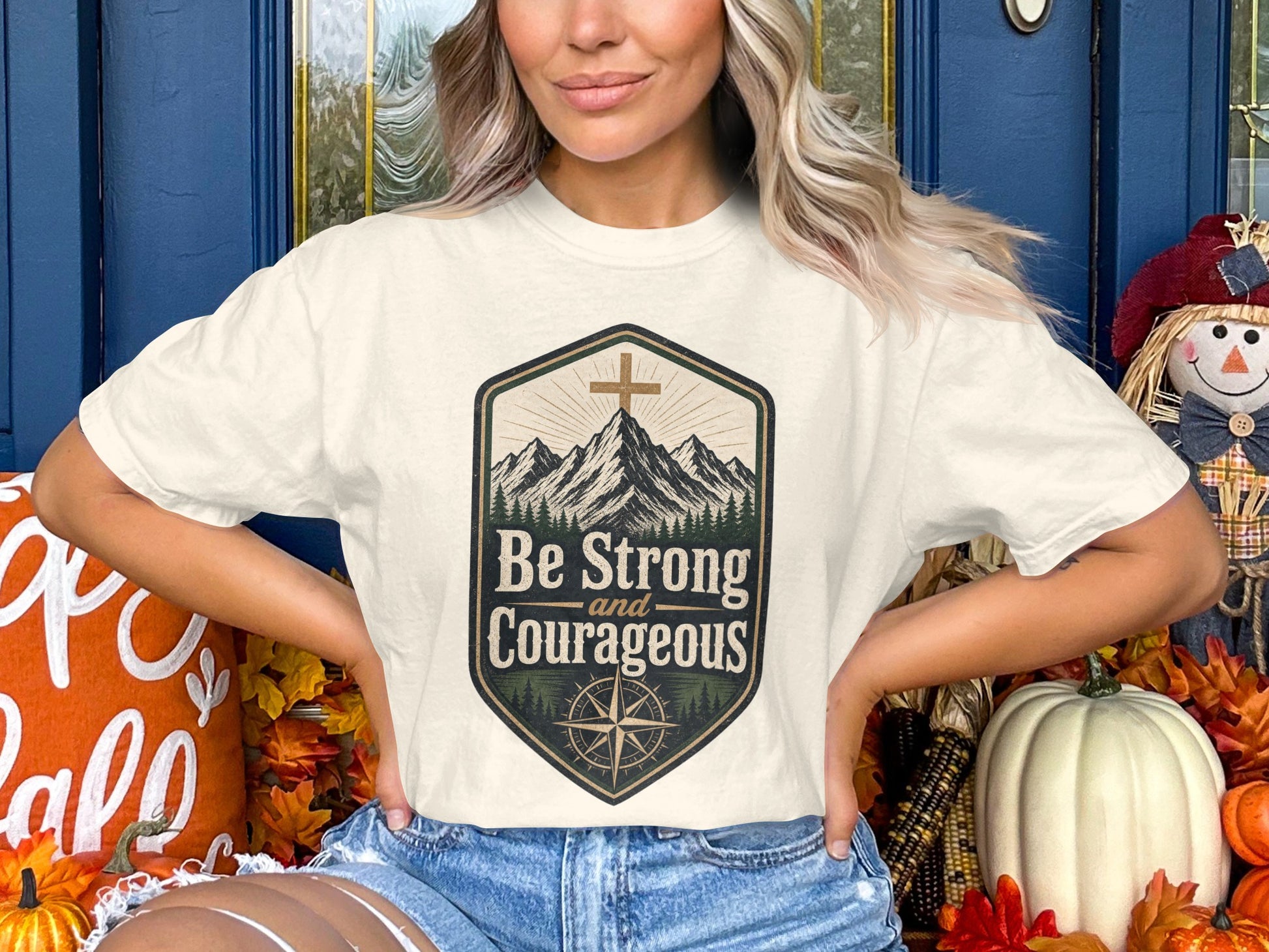 Cream t-shirt with mountains, compass, and "Be Strong and Courageous" text.