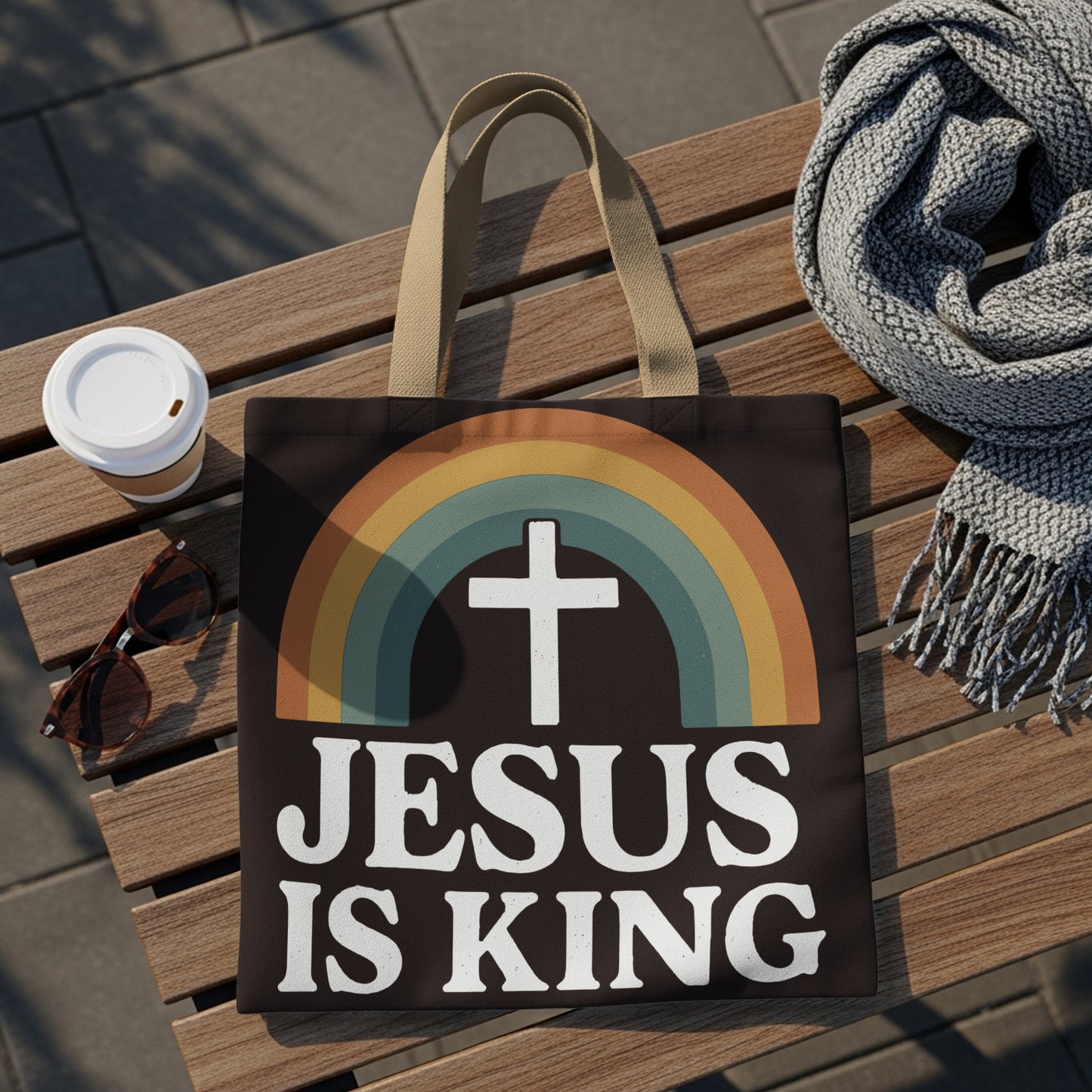 Dark tote bag with white text "JESUS IS KING" and a cross inside a rainbow.