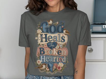 Dark gray t-shirt with "God Heals The Broken Hearted" text and floral embellishments.