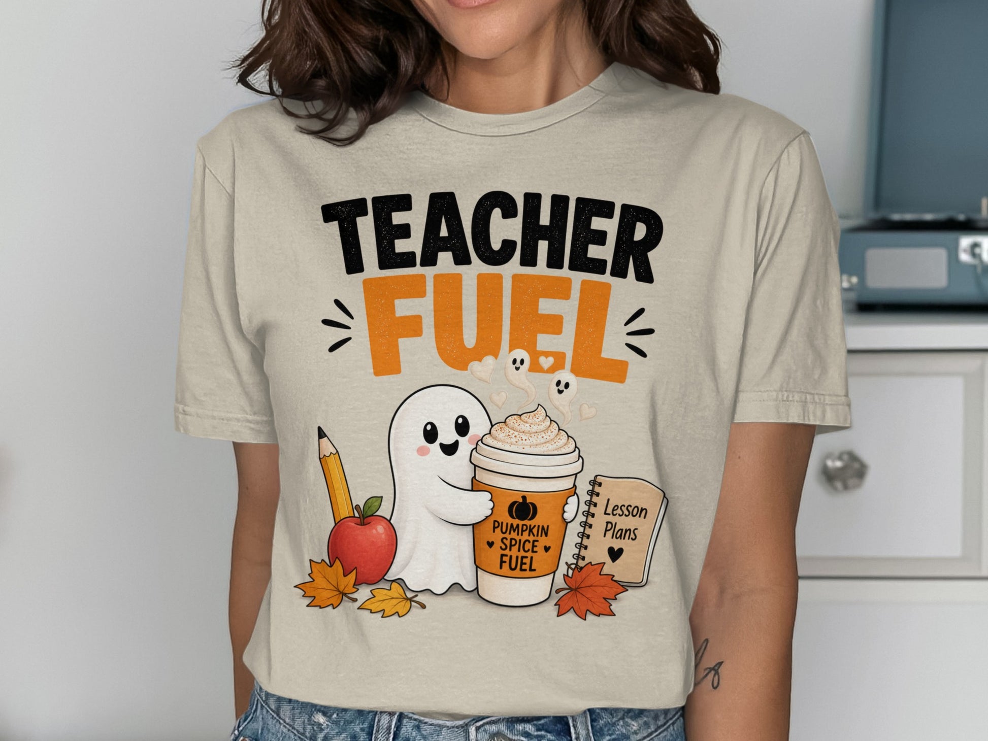 T-shirt graphic with "Teacher Fuel" text, a ghost, pumpkin spice coffee, apple, pencil, and lesson plans.