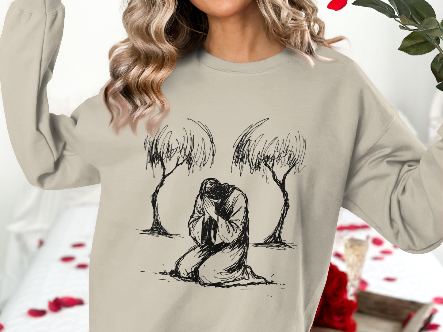 Woman wearing beige sweatshirt with kneeling figure and trees illustration.