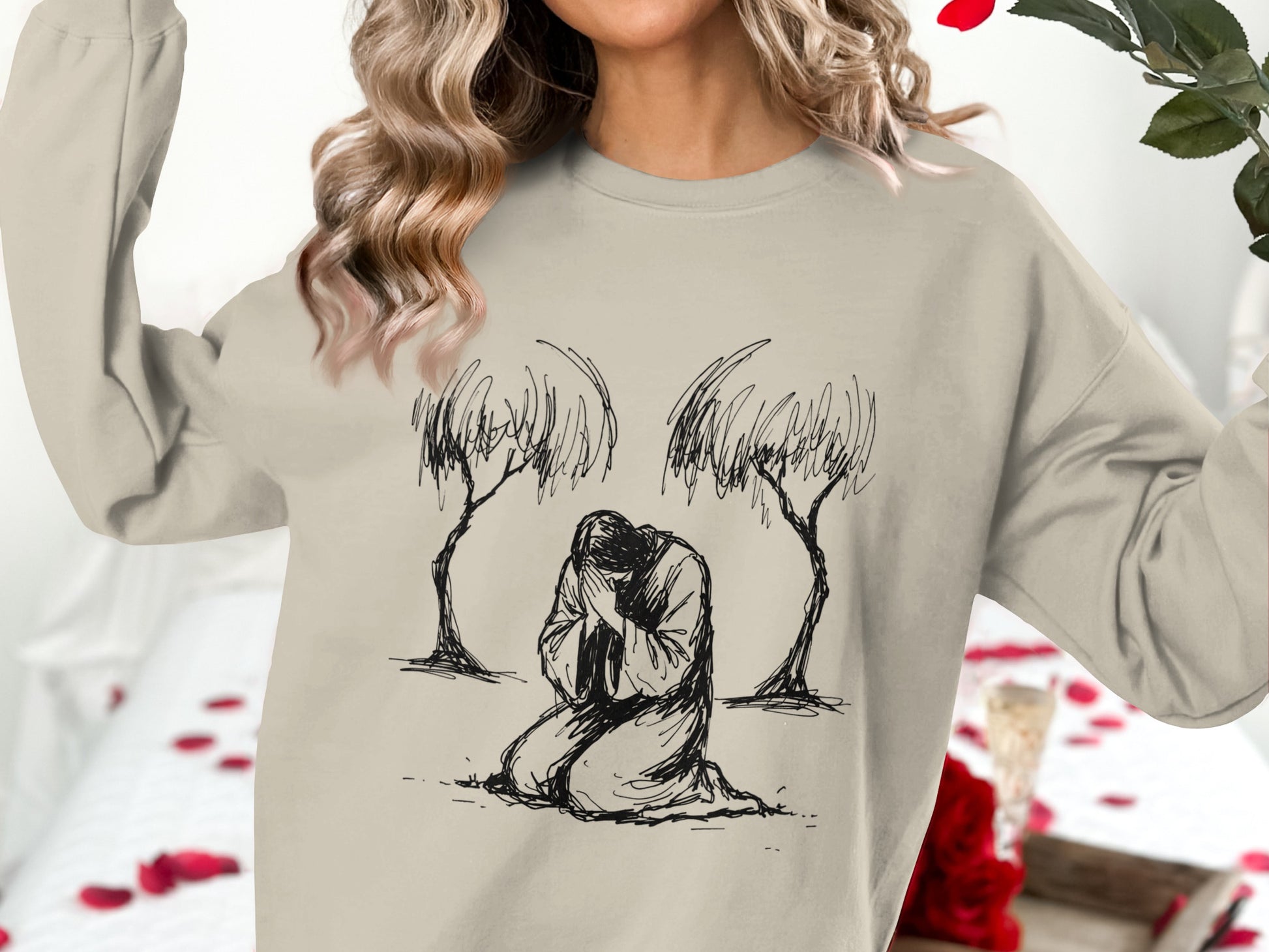 Woman wearing beige sweatshirt with kneeling figure and trees illustration.