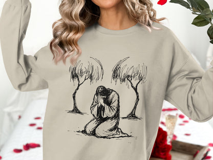 Woman wearing beige sweatshirt with kneeling figure and trees illustration.
