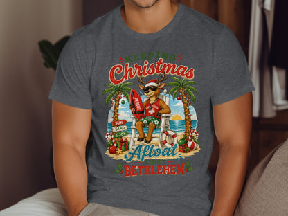 Deer lifeguard in Santa hat with surfboard on beach, text "Keeping Christmas Afloat Since Bethlehem".
