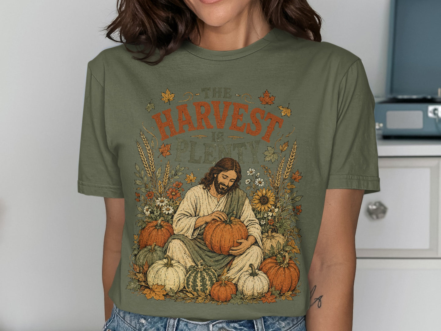 Olive green t-shirt with Jesus holding a pumpkin, surrounded by harvest-themed illustrations.