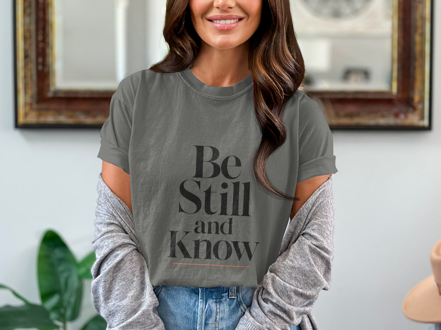 Gray t-shirt with black text "Be Still and Know" and an orange line.