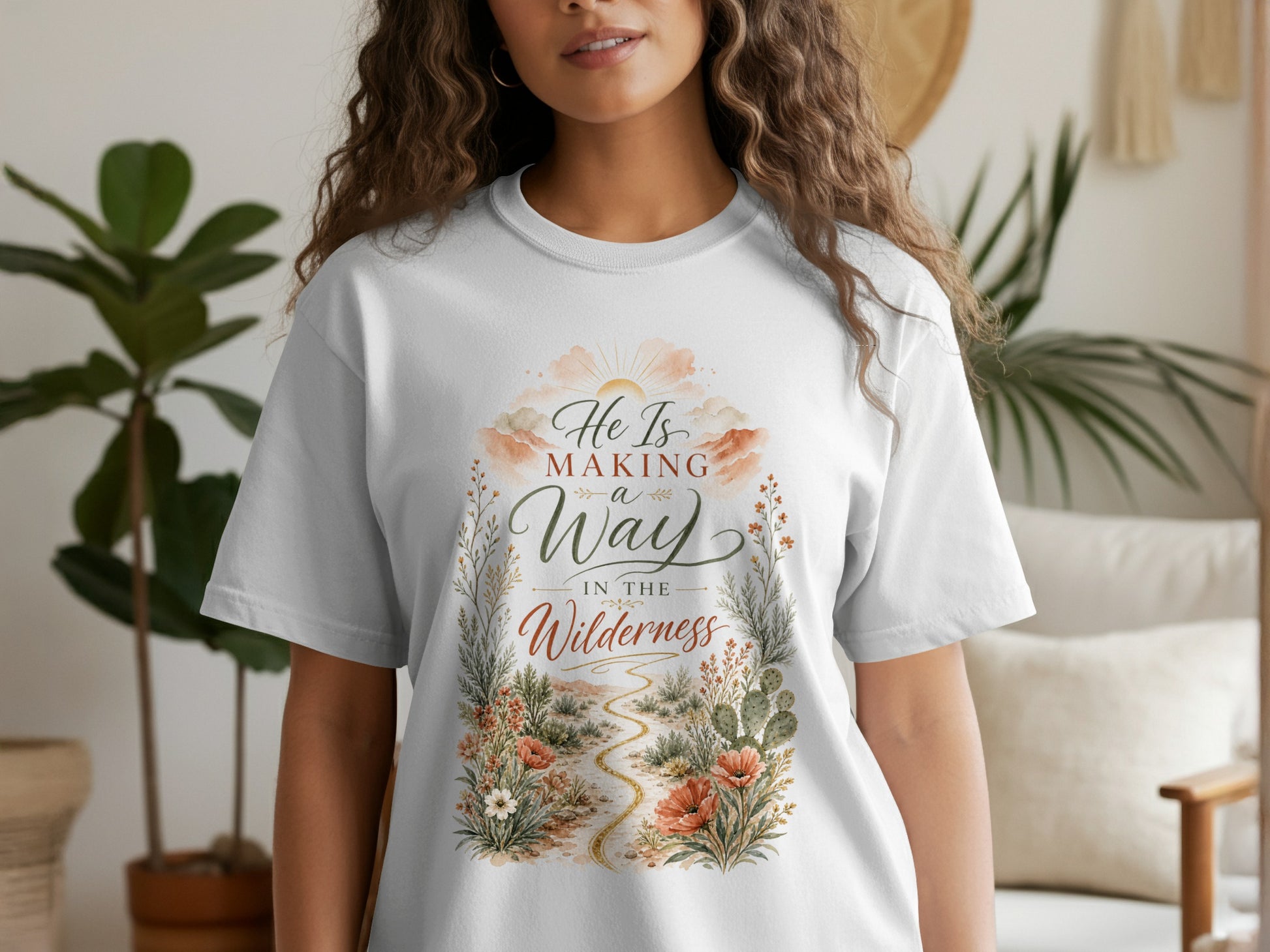 White t-shirt with graphic art of sun, clouds, path, and text "He Is Making a Way in the Wilderness."