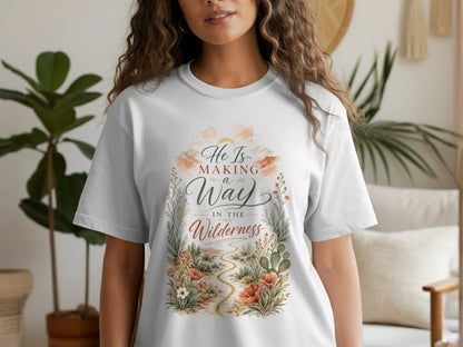White t-shirt with graphic art of sun, clouds, path, and text "He Is Making a Way in the Wilderness."