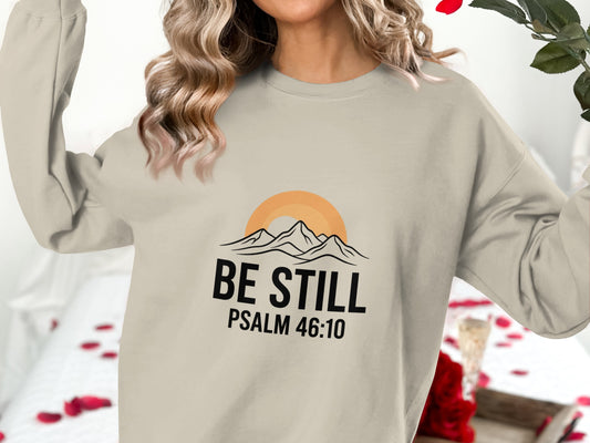 Crewneck sweatshirt with "BE STILL PSALM 46:10" and mountain sunrise graphic.