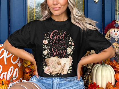 Black t-shirt with "God Is Still Writing My Story" text and floral design.