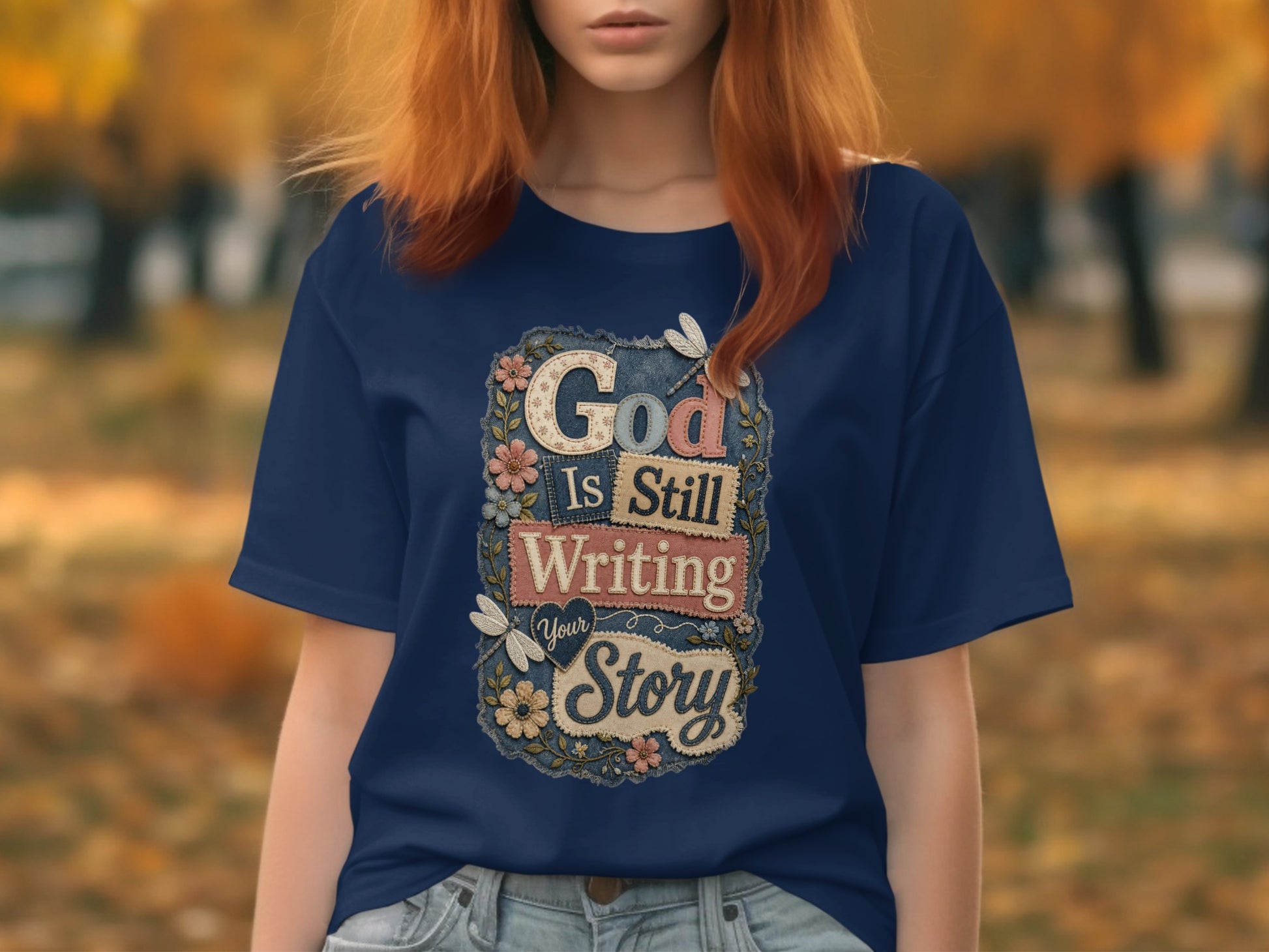 Navy t-shirt with "God Is Still Writing Your Story" text and floral accents.