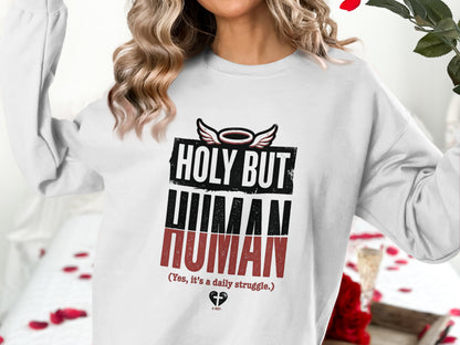 White sweatshirt with "HOLY BUT HUMAN" text and graphic design.