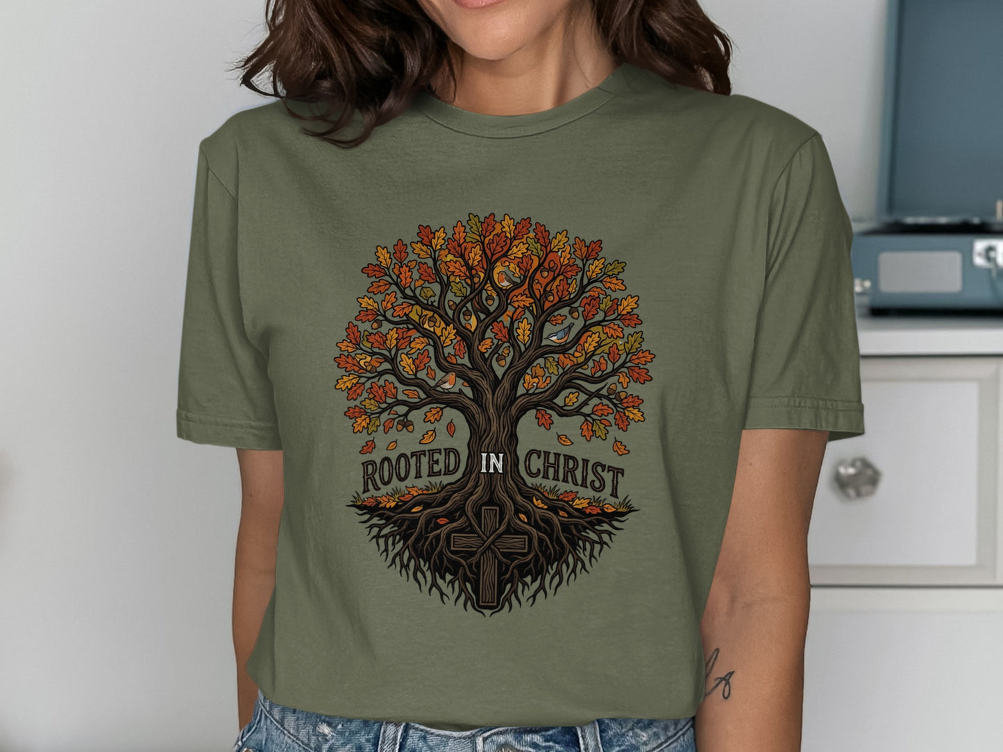 Olive green t-shirt with tree of life design and "Rooted in Christ" text.