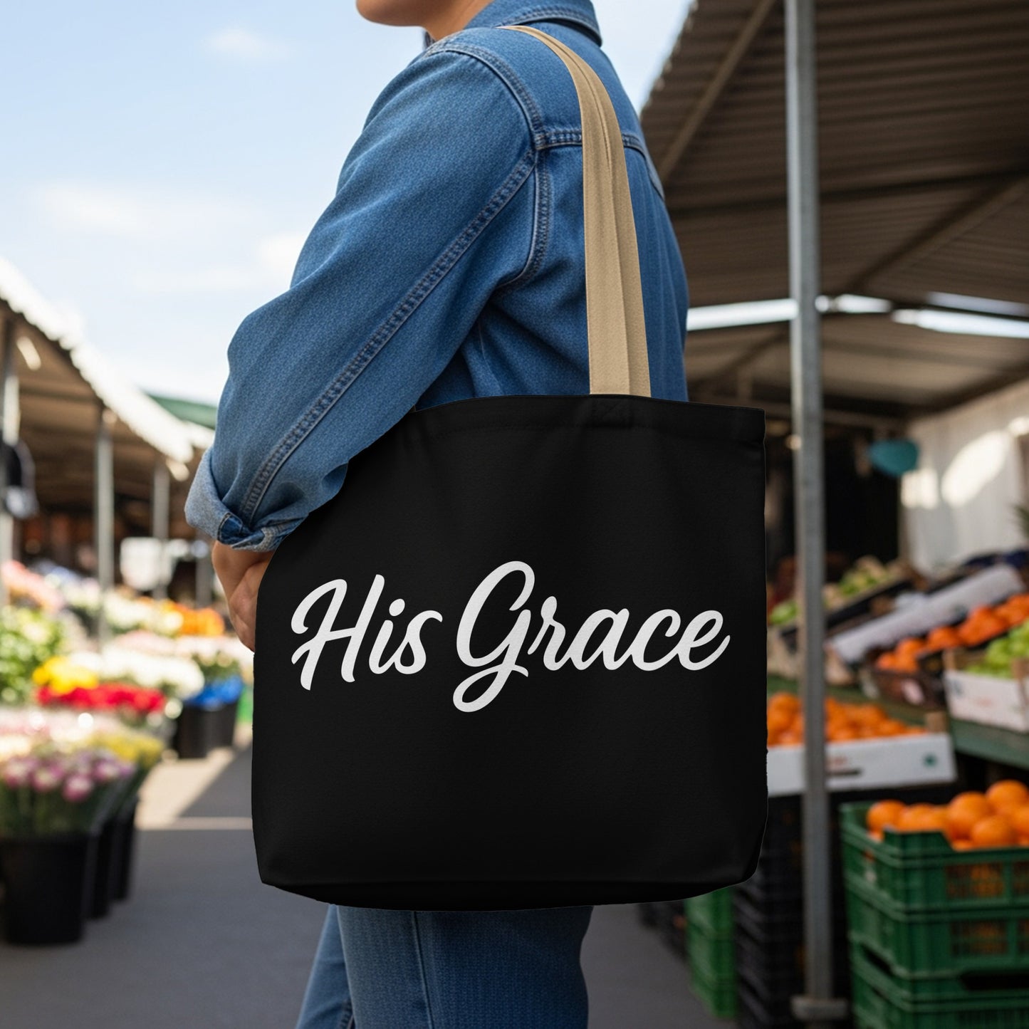 Black tote bag with white script text "His Grace" held by a person outdoors.