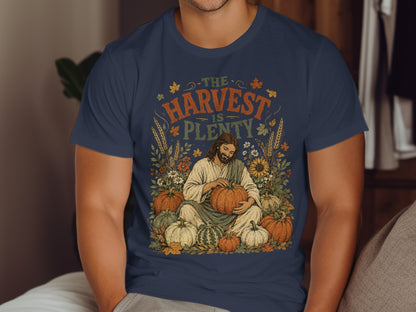 Jesus sitting amongst pumpkins and fall foliage with text "The Harvest is Plenty".