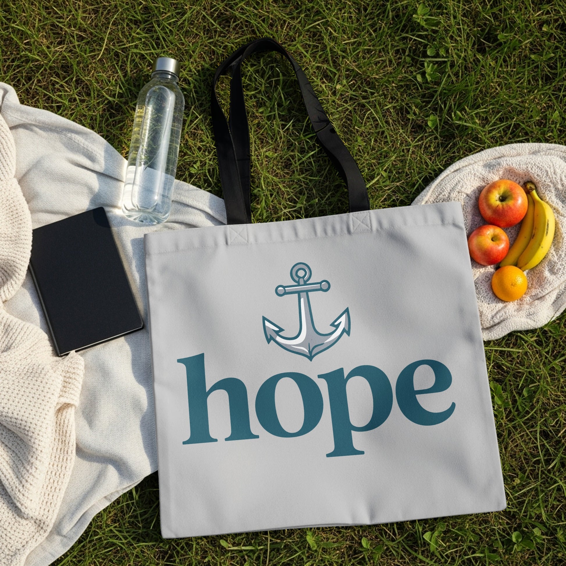 Tote bag with anchor and "hope" text on a grassy picnic blanket.