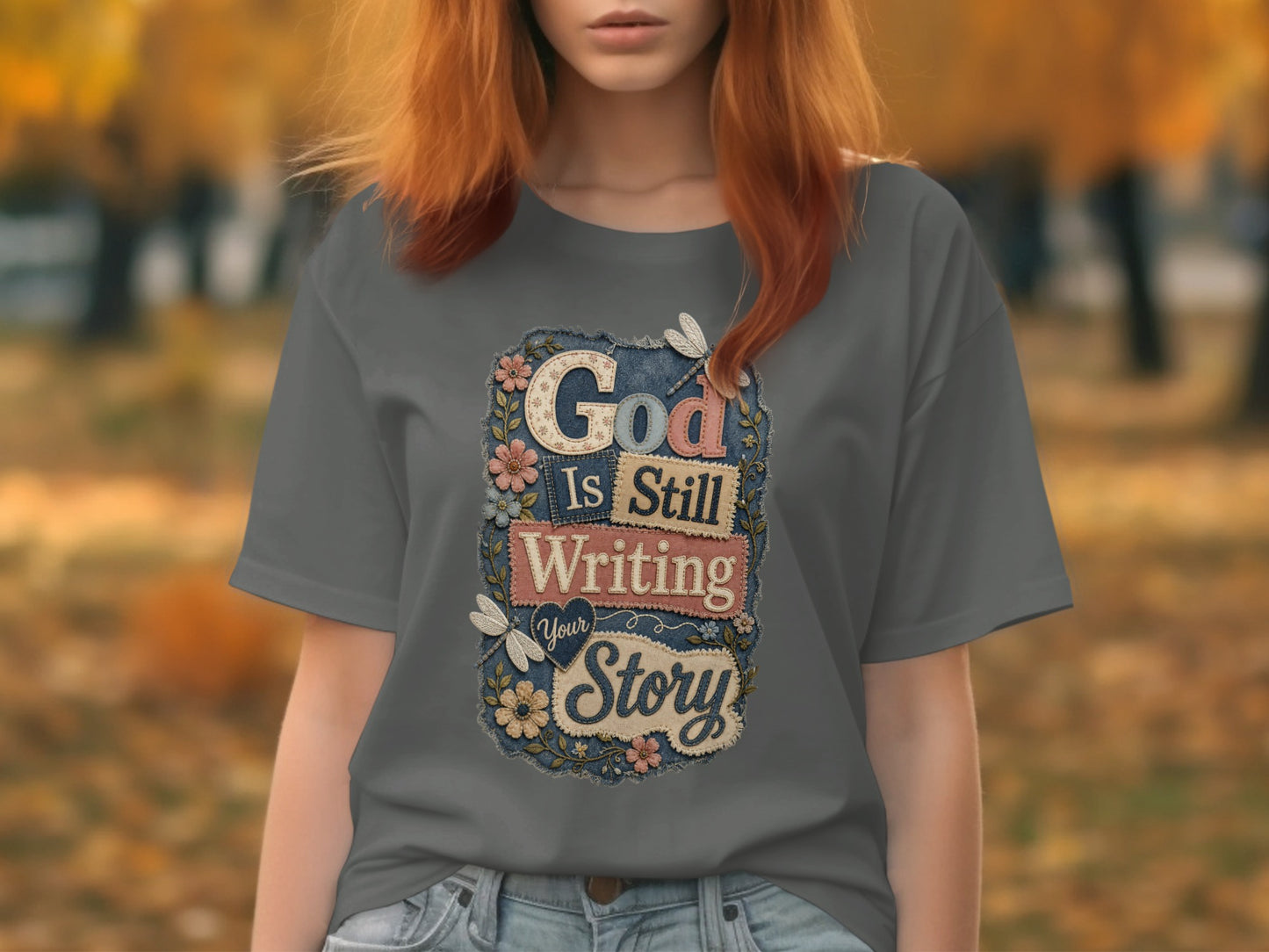Gray t-shirt with "God Is Still Writing Your Story" text and floral accents.