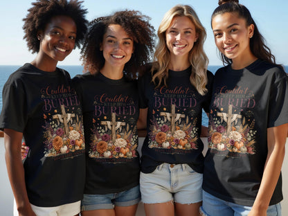 Four women model black t-shirts with a floral cross design and text reading "Couldn't Keep Him Buried."
