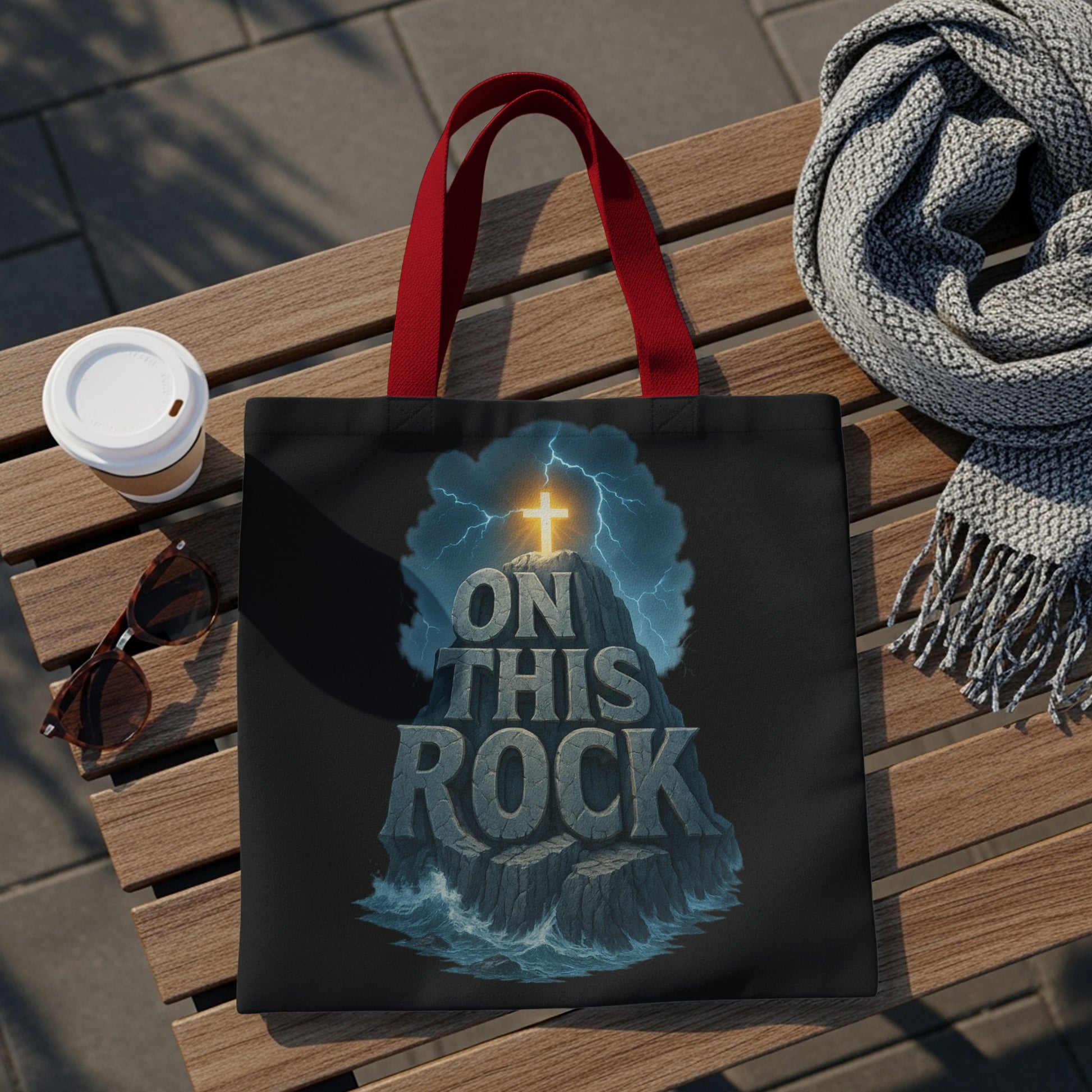 Black tote bag with glowing cross, "ON THIS ROCK" text, and stormy sea design.