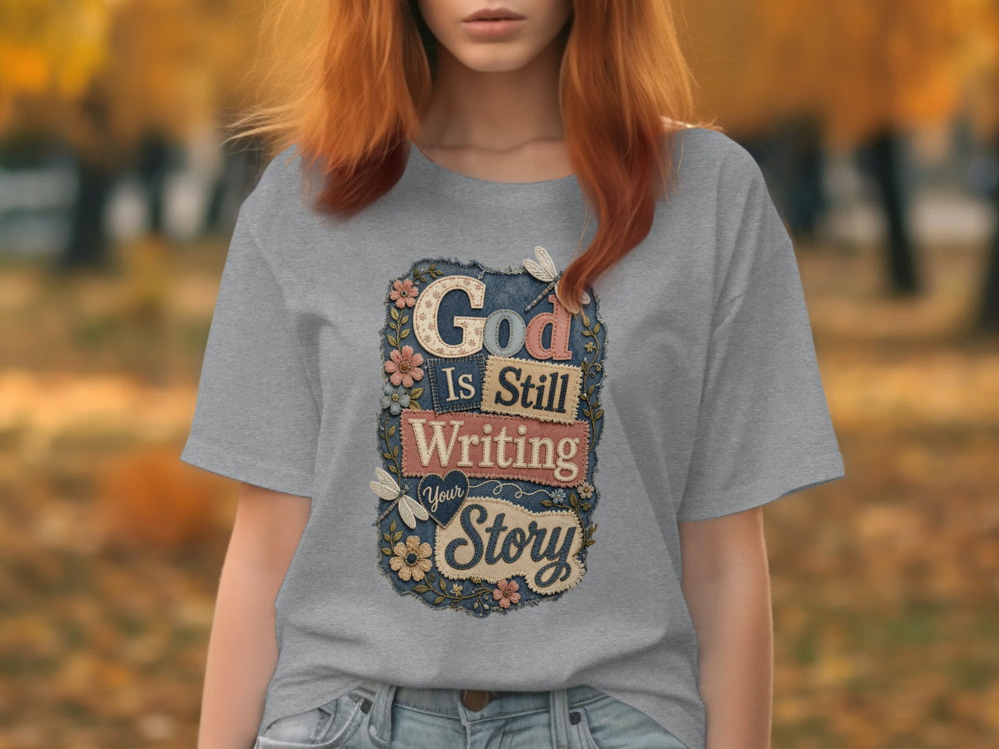 Grey t-shirt with "God Is Still Writing Your Story" text and floral accents.