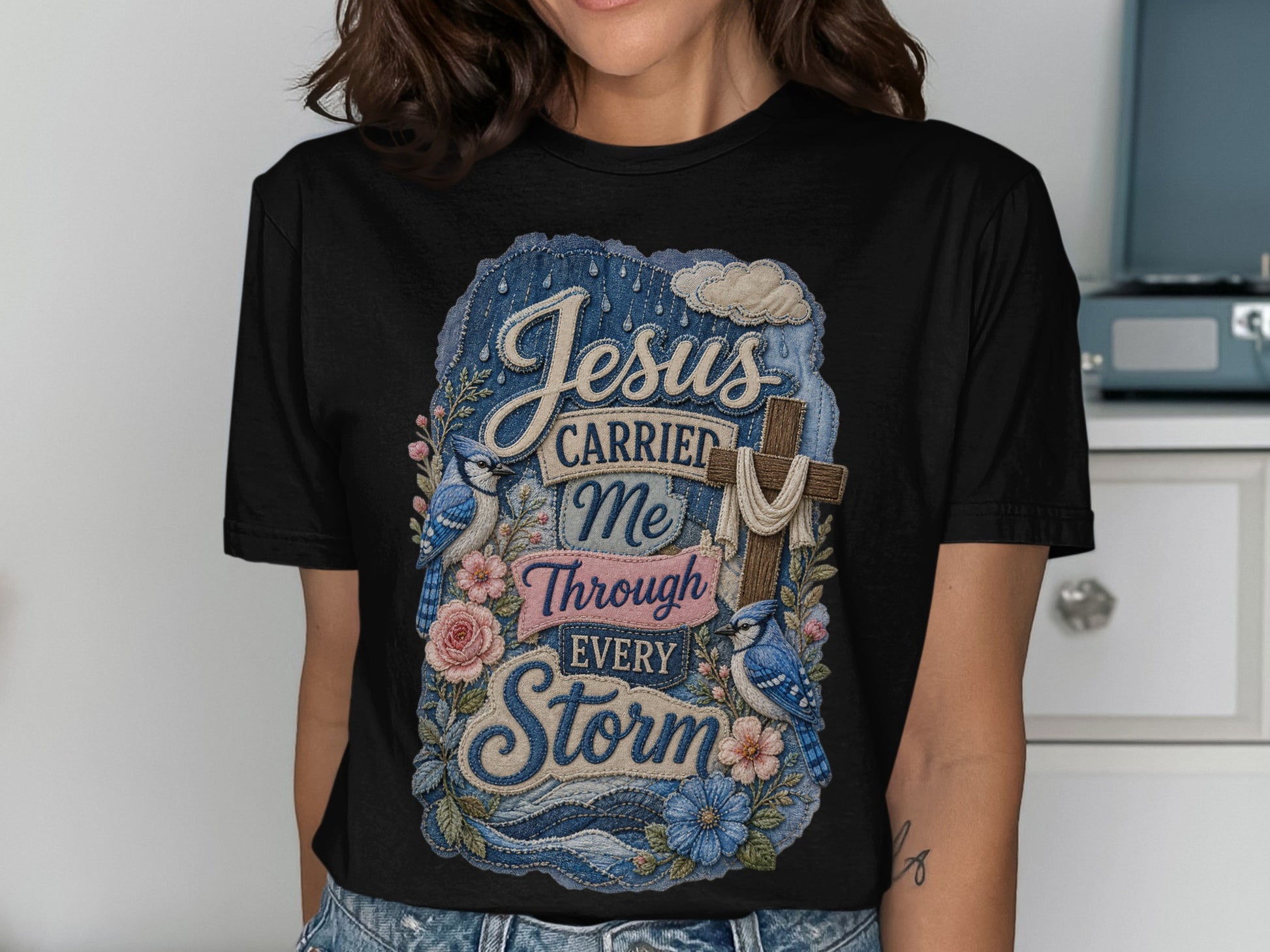 Black t-shirt with "Jesus Carried Me Through Every Storm" text and floral design.