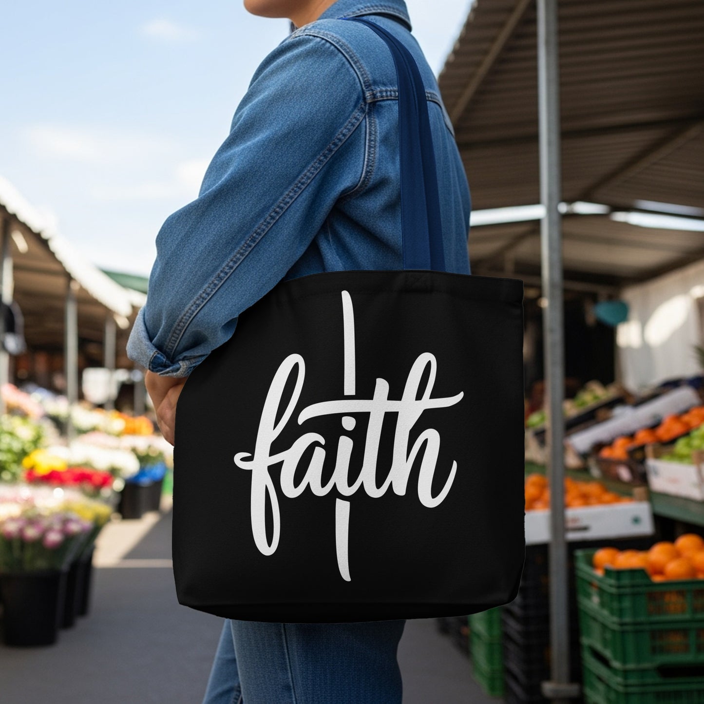 Black tote bag with white "faith" text held by a person wearing a denim jacket.