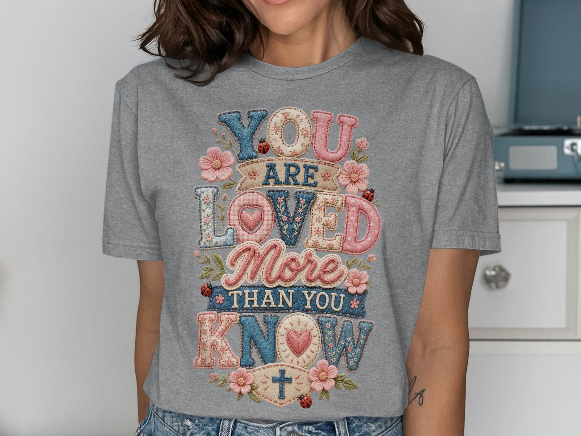 Gray t-shirt with "YOU ARE LOVED MORE THAN YOU KNOW" text in patchwork font.