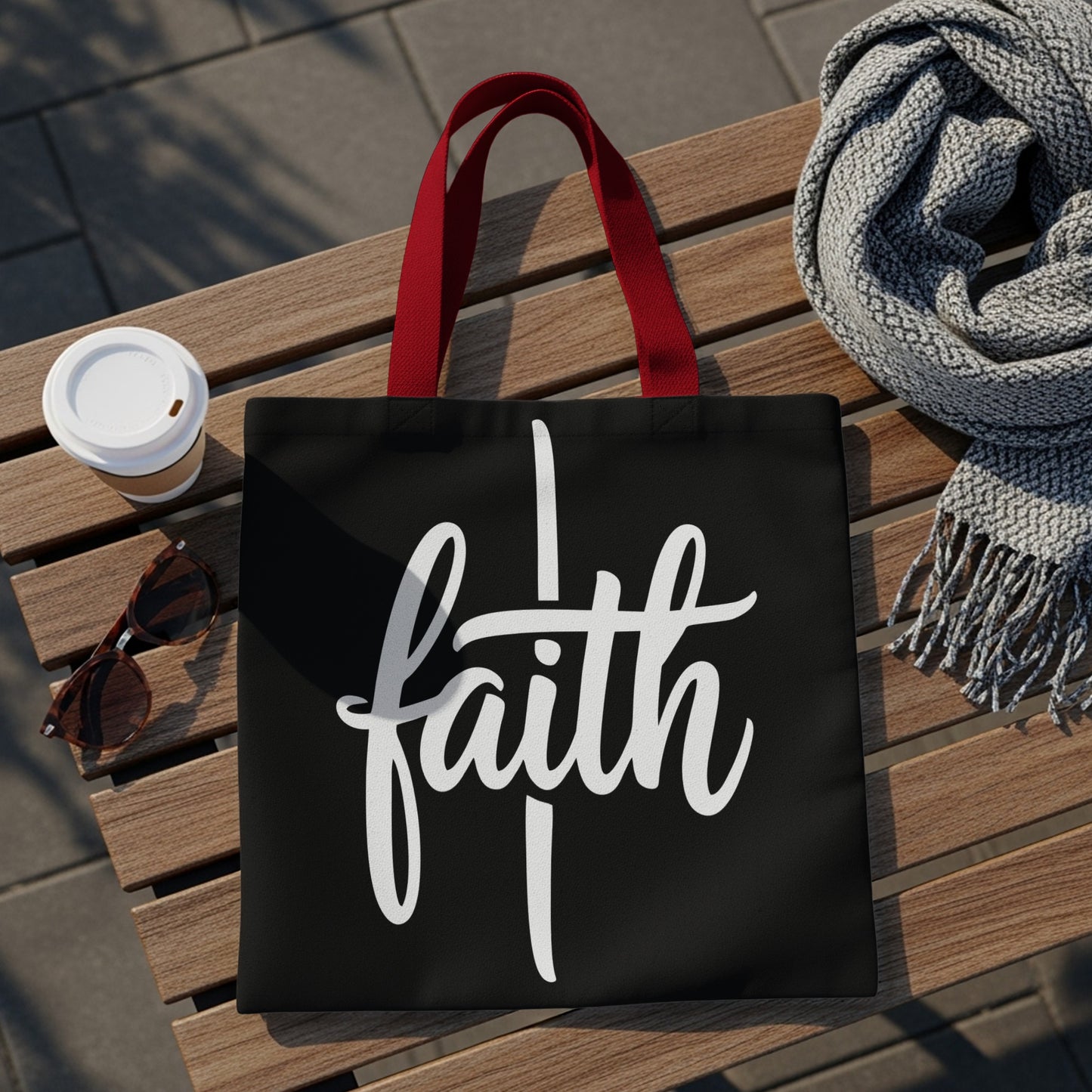 Black tote bag with white "faith" text and red straps, on a bench.