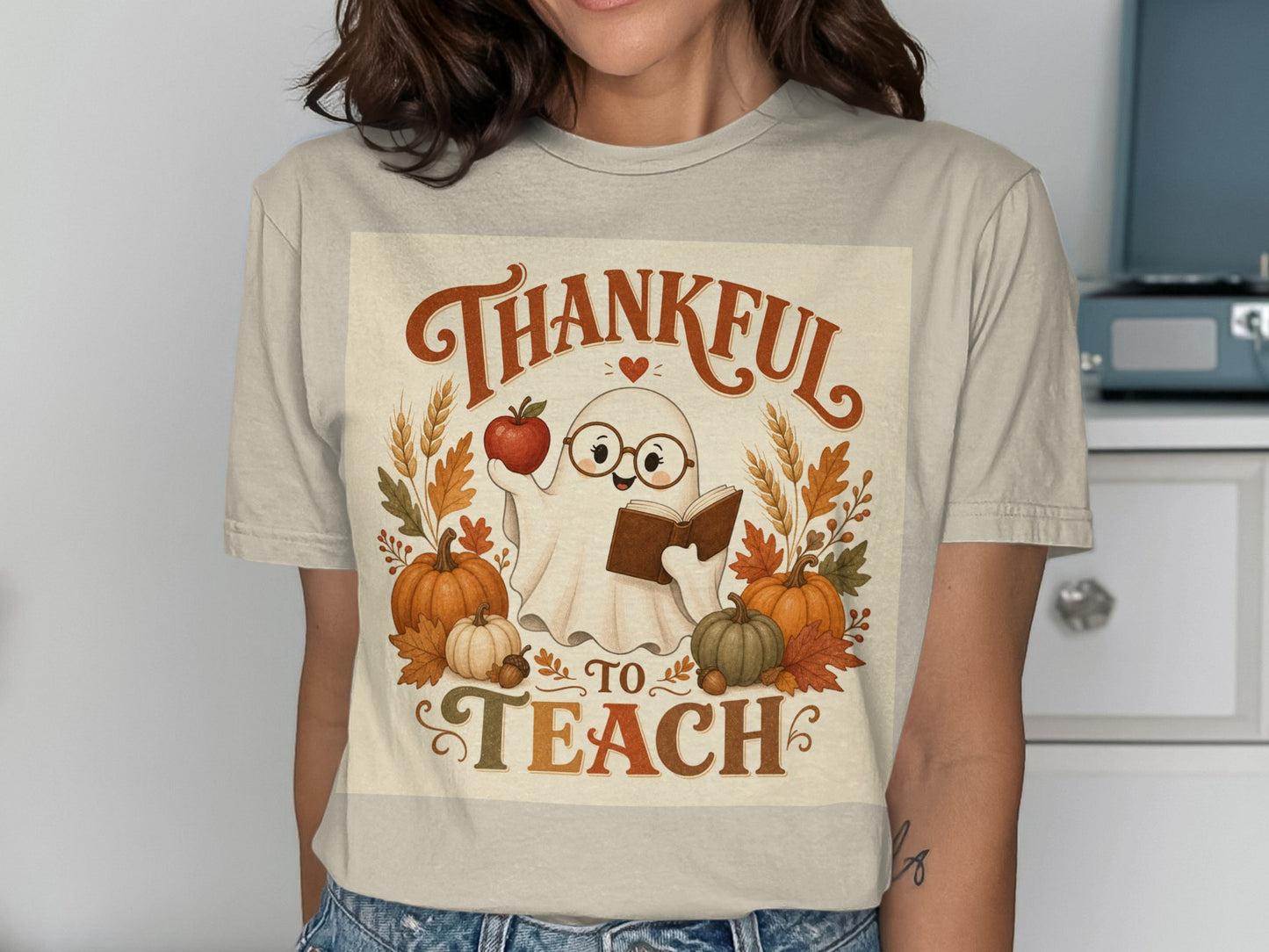 Ghost character holding book and apple, text "Thankful to Teach", pumpkins, and fall leaves.