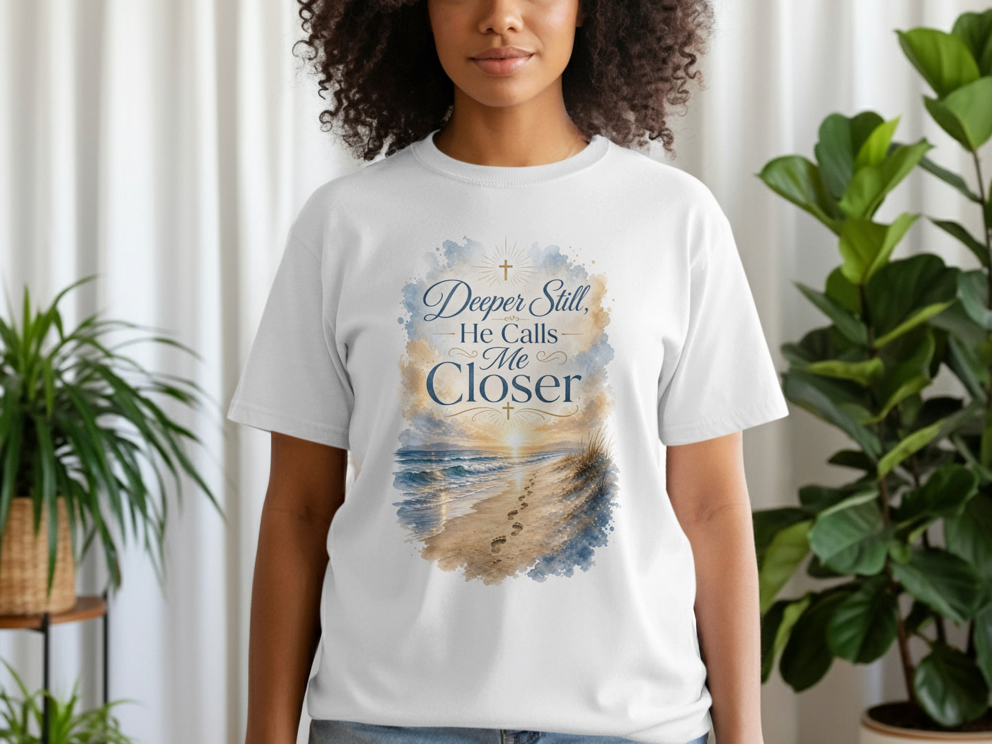 White t-shirt with watercolor beach sunset design and text "Deeper Still, He Calls Me Closer".