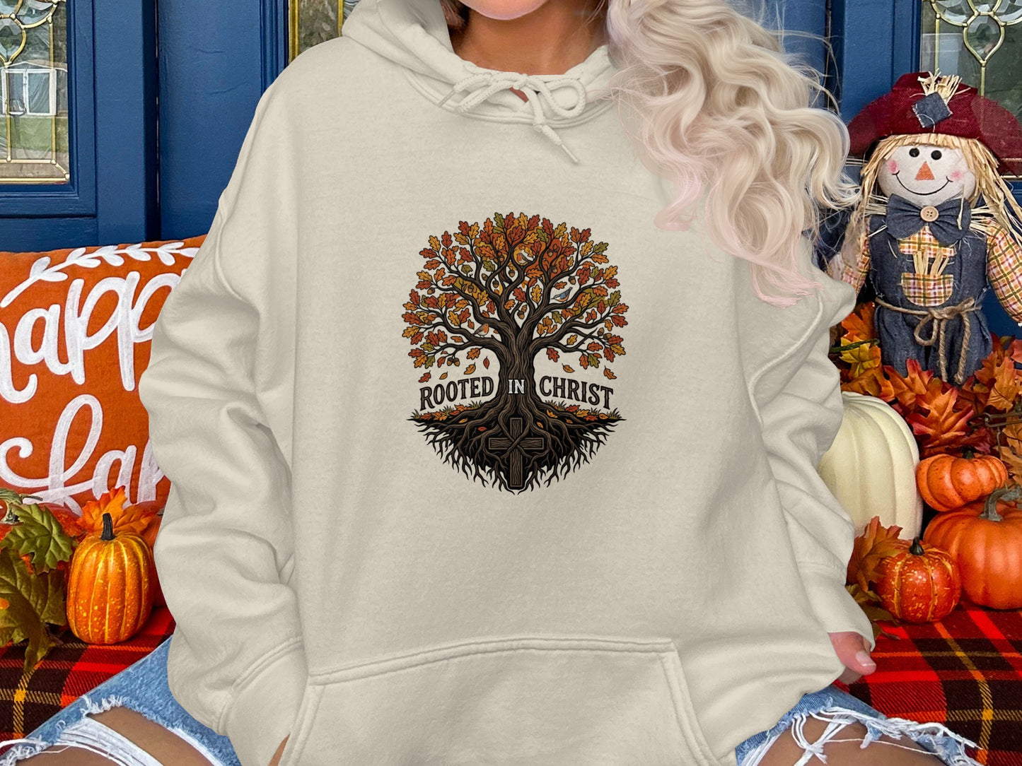 Cream hoodie with "Rooted in Christ" tree design, surrounded by fall decorations.