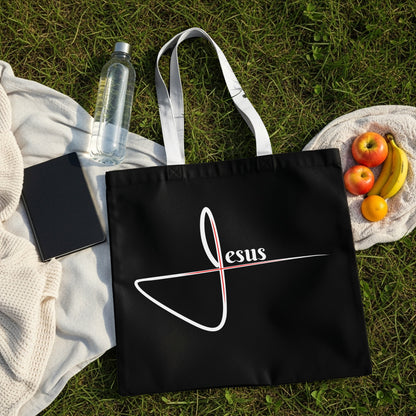Black tote bag with "Jesus" text and a graphic on a grassy background.