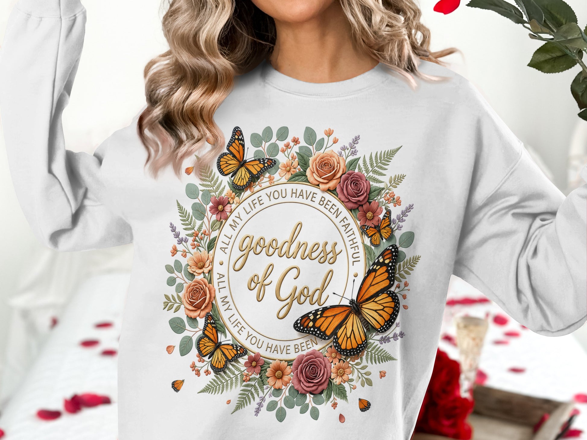 White sweatshirt with floral wreath, butterflies, and "goodness of God" text.