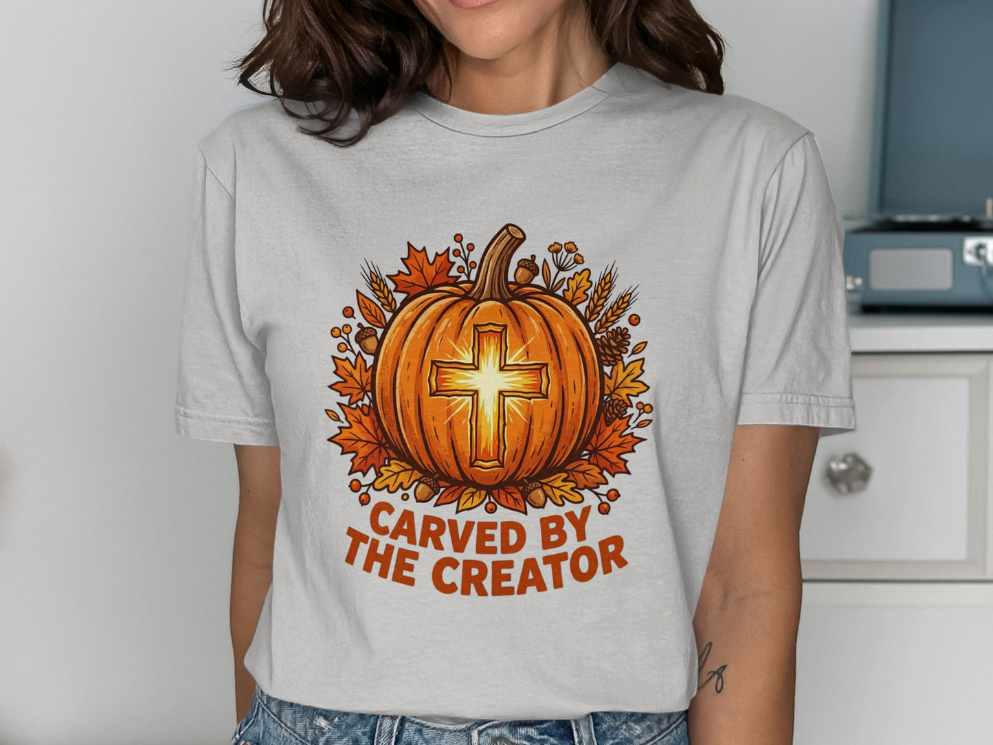 Pumpkin with cross design, "Carved by the Creator" text, surrounded by autumn leaves.
